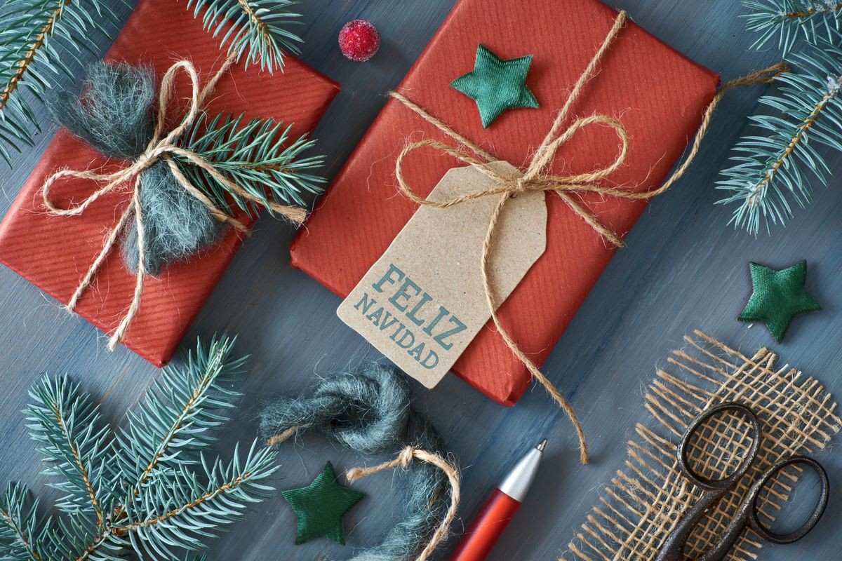 Rustic wooden background with fir branches and Christmas presents gift wrapped in red paper. Flat lay, top view, text "Feliz Navidad" (Merry Christmas in Spanish) on the cardboard tag